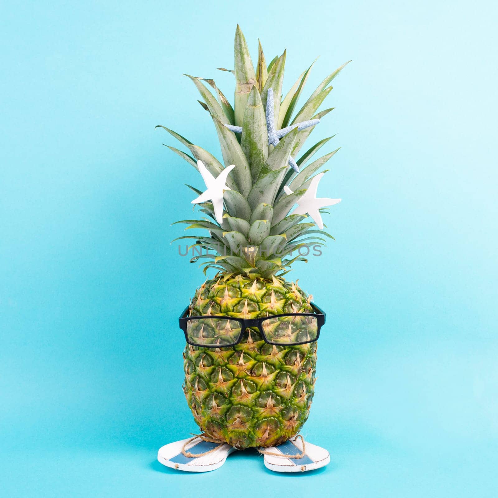 Pineapple with glasses and flip flops, vacation and travel concept, tropical summer holiday, funny fruit, blue background