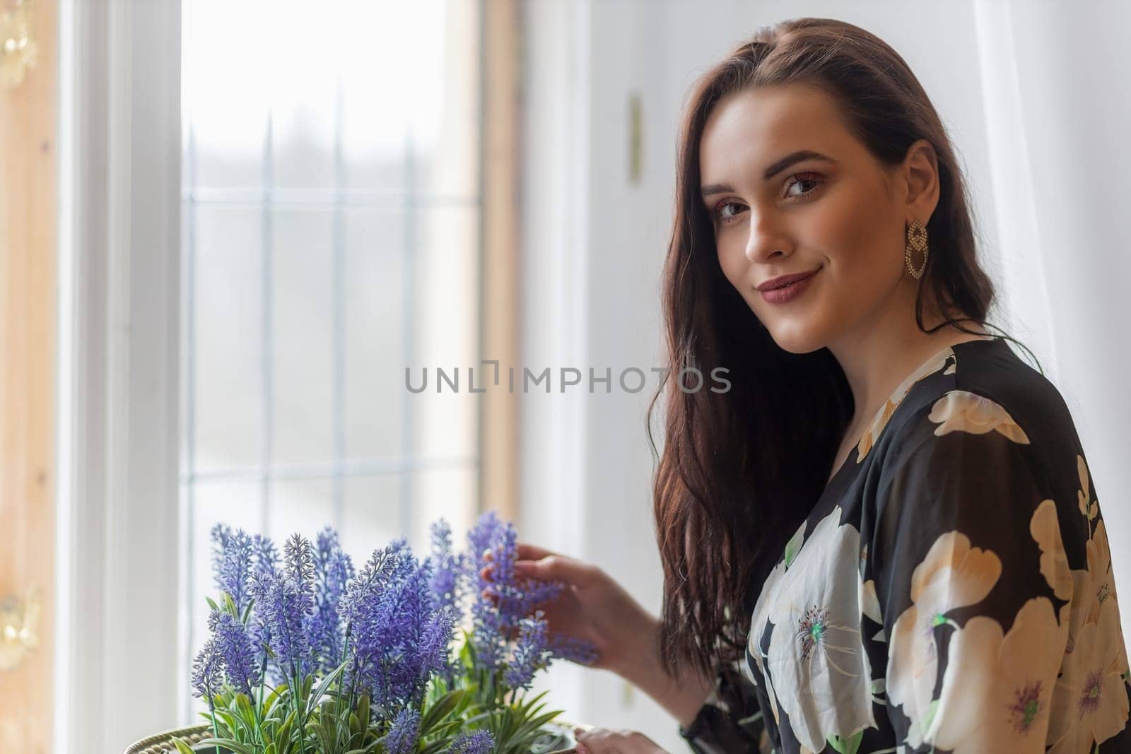 Attractive dark haired girl is holding  purple flowers in a pot. Horizontally.