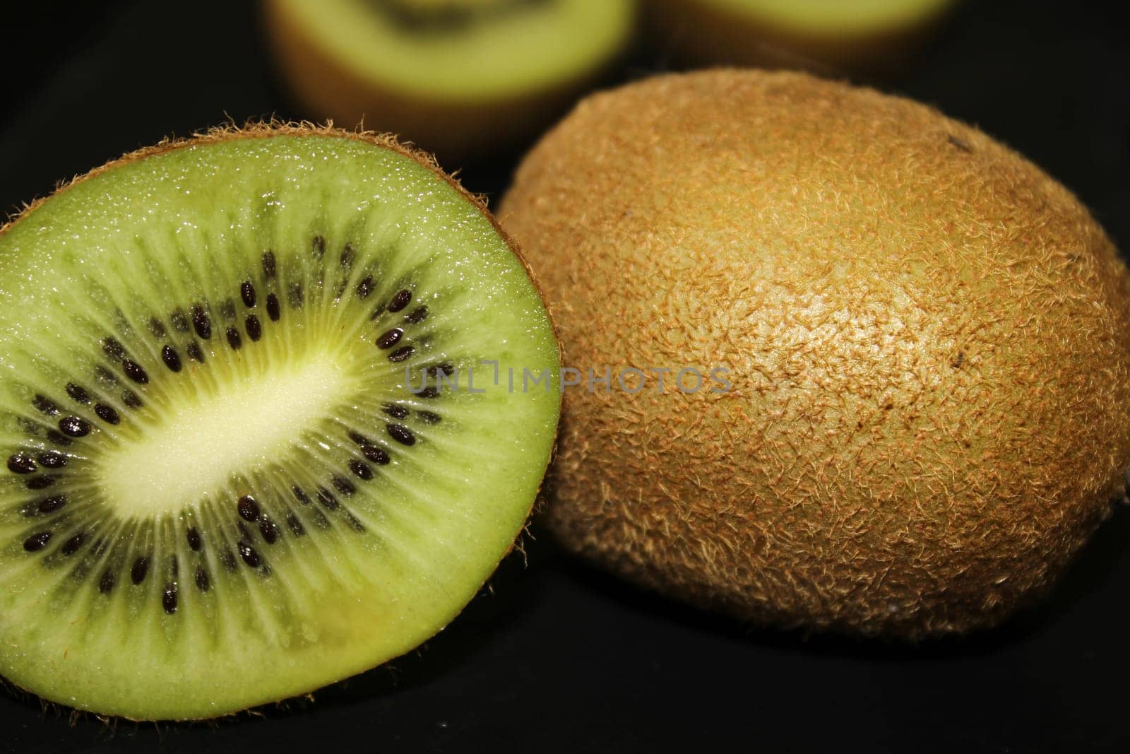 Half a kiwi and a whole kiwi close-up on a black background..