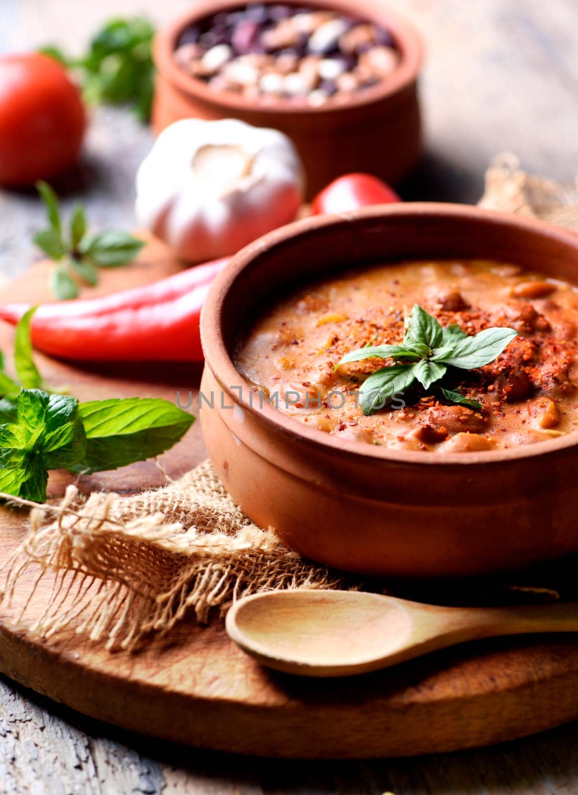Traditional homemade recipe for spicy baked beans cooked in vintage clay bowl with vegetable and herbs.
