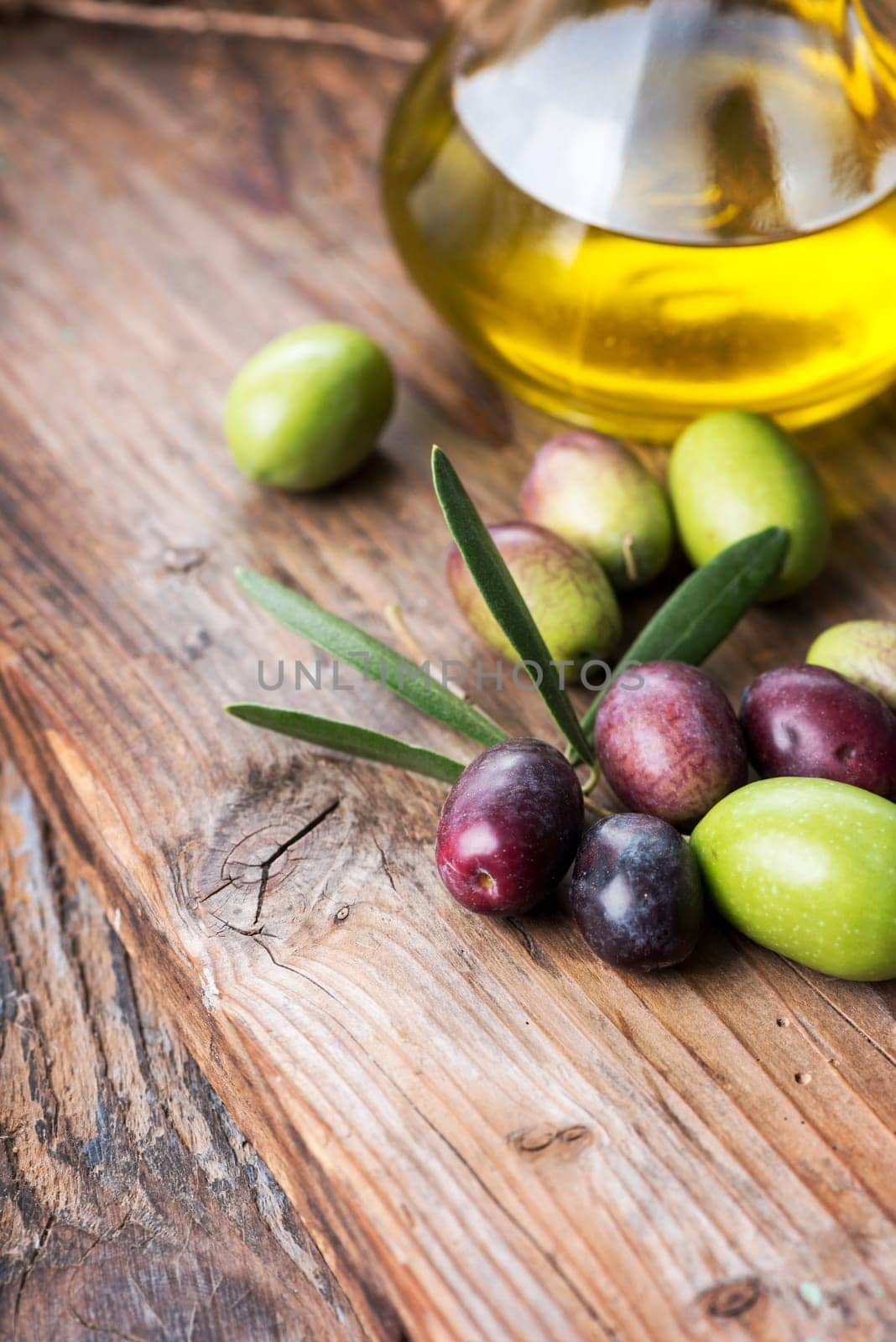 Fresh olives and extra virgin olive oil bottle on wooden textured board.