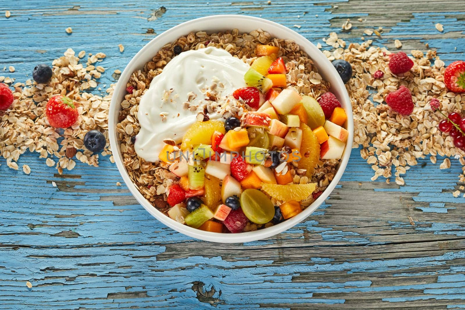 Top view of tasty oat with fruits and berries in bowl prepared for breakfast and placed on wooden table