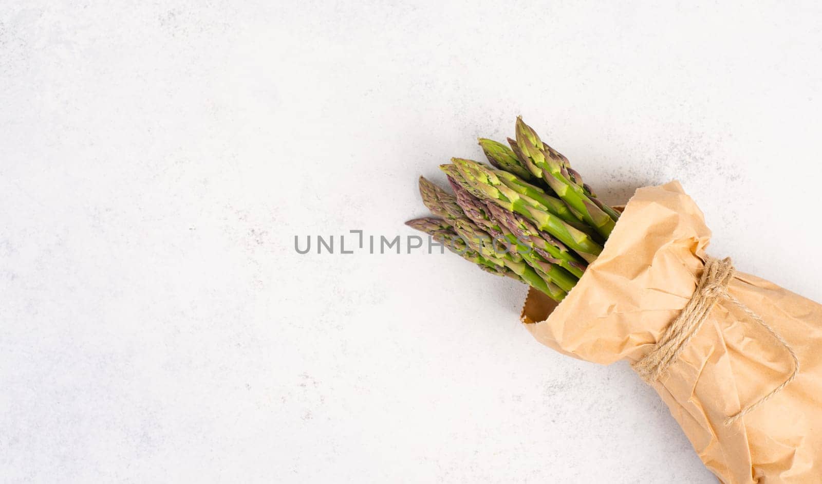 Fresh green bundle of asparagus on a white textured table, vegetables in spring, gourmet cuisine food, cooking a vegan meal