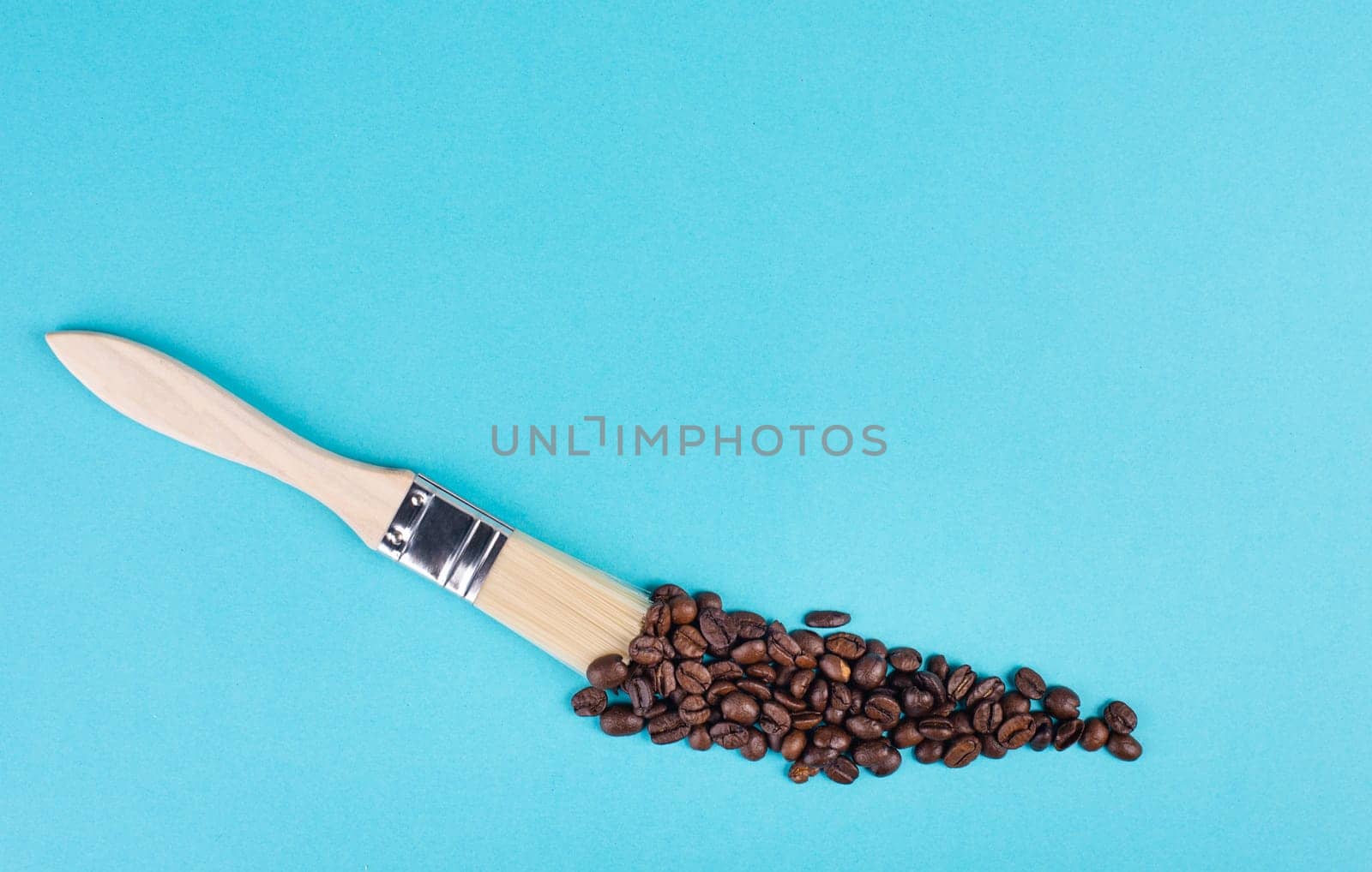 Painting with a brush a line with roasted coffee beans, blue background with copy space, having a hot drink for breakfast, taking a break