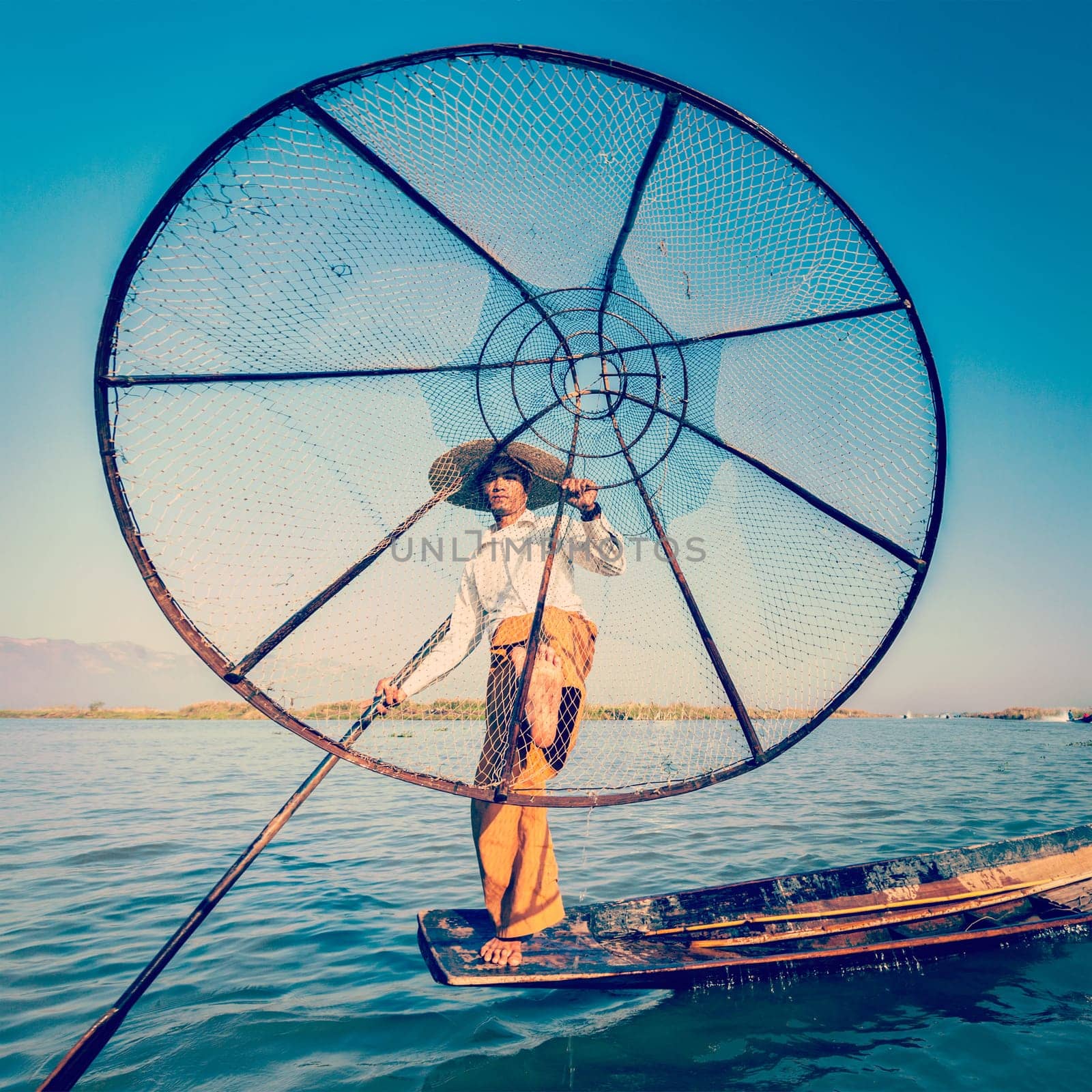 Vintage retro effect filtered hipster style image of Myanmar travel attraction. Traditional Burmese fisherman with fishing net at Inle lake famous for their distinctive one legged rowing style