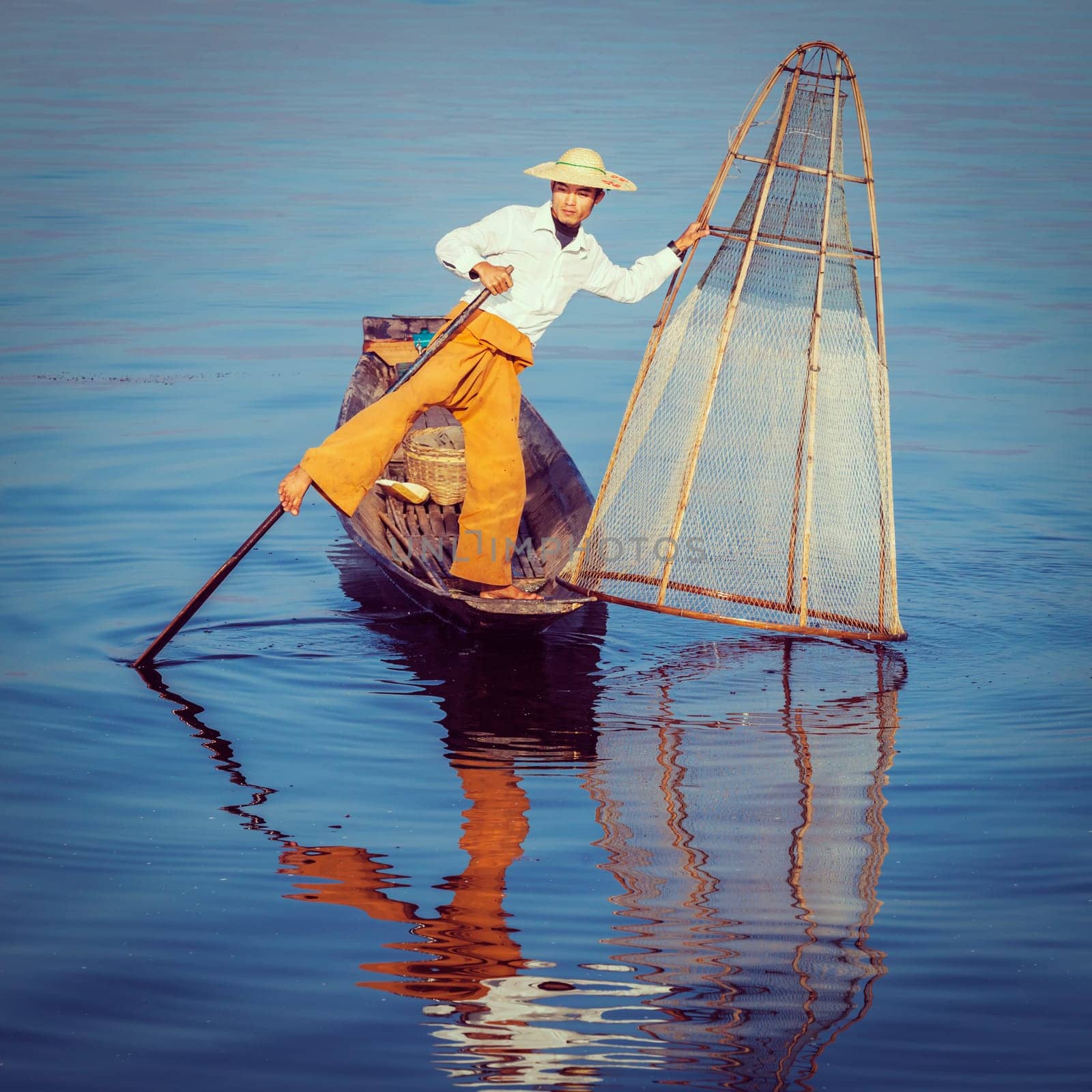 Vintage retro effect filtered hipster style image of Myanmar travel attraction. Traditional Burmese fisherman with fishing net at Inle lake famous for their distinctive one legged rowing style