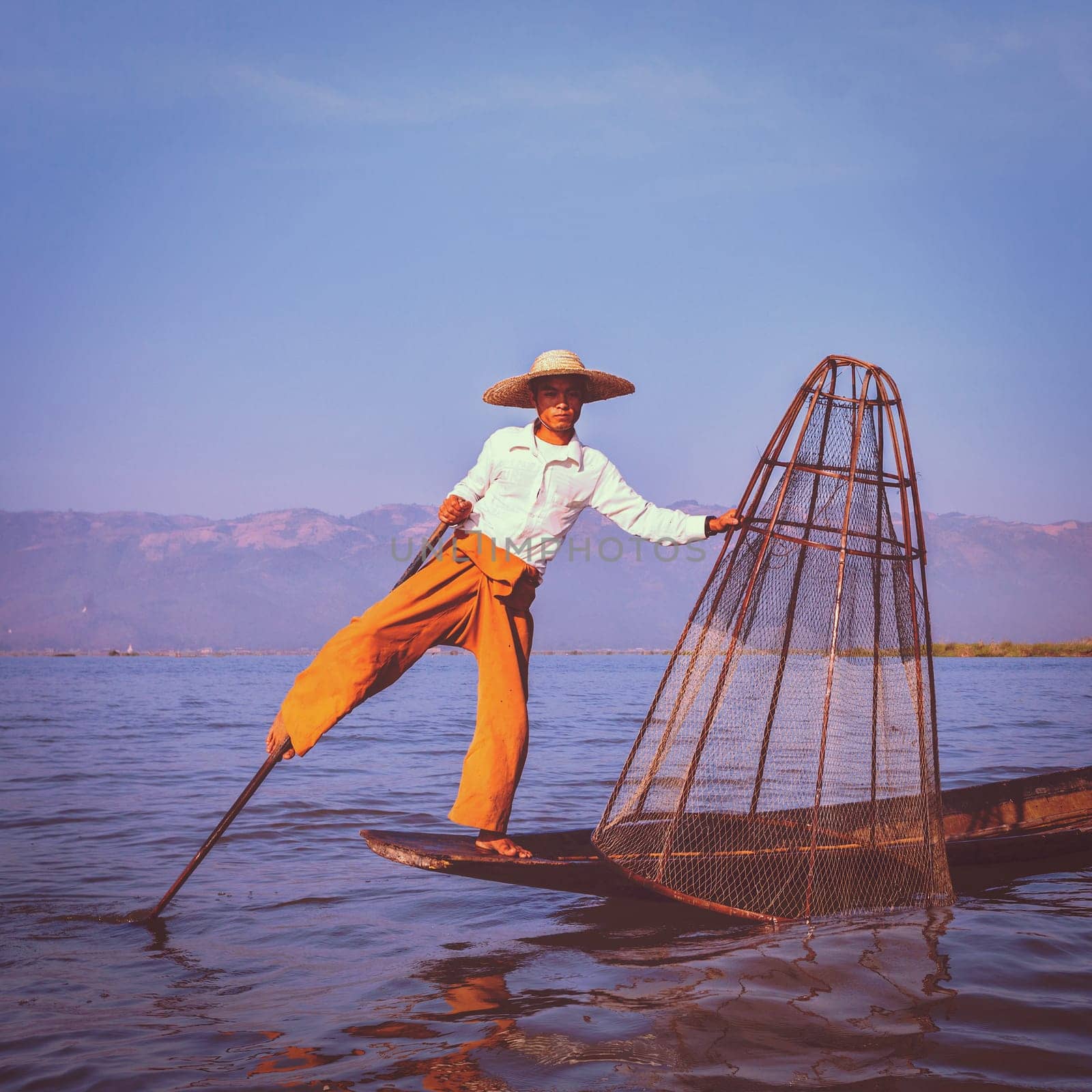 Vintage retro effect filtered hipster style image of Myanmar travel attraction. Traditional Burmese fisherman with fishing net at Inle lake famous for their distinctive one legged rowing style