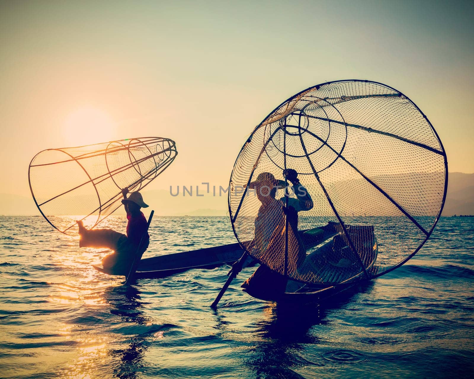 Myanmar travel toursist attraction landmark - two traditional Burmese fishermen at Inle lake, Myanmar on sunrise. Vintage filtered retro effect hipster style image