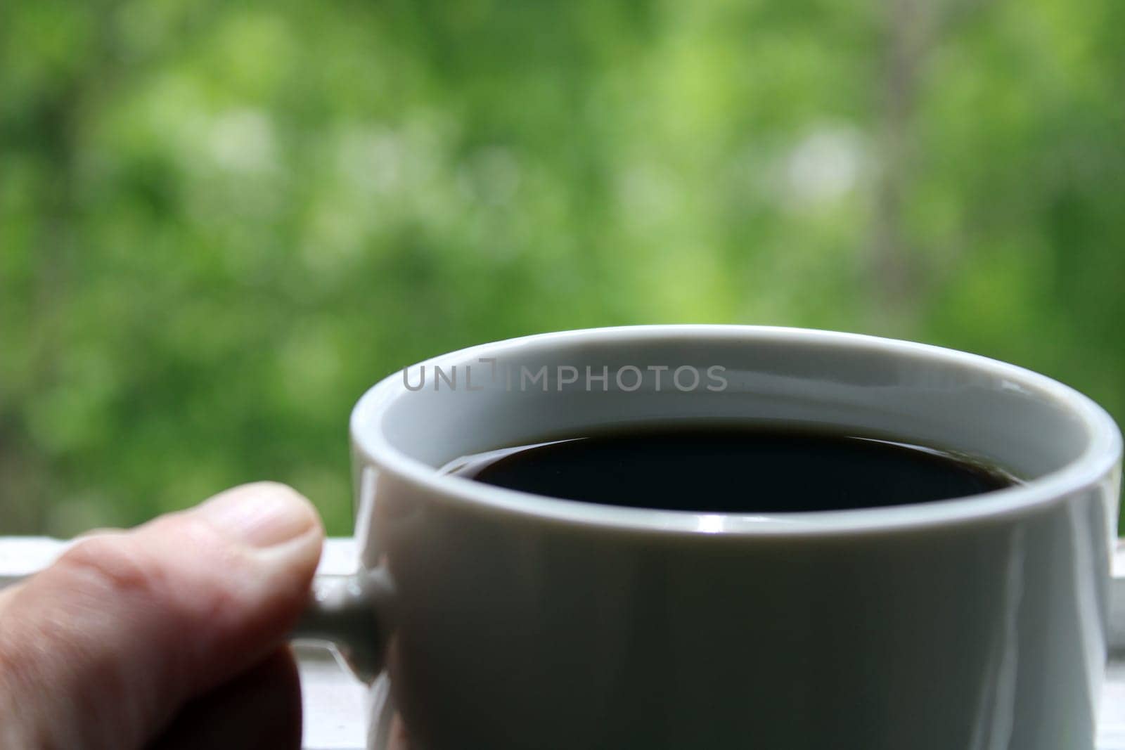 White mug with black coffee close-up on a natural green background..