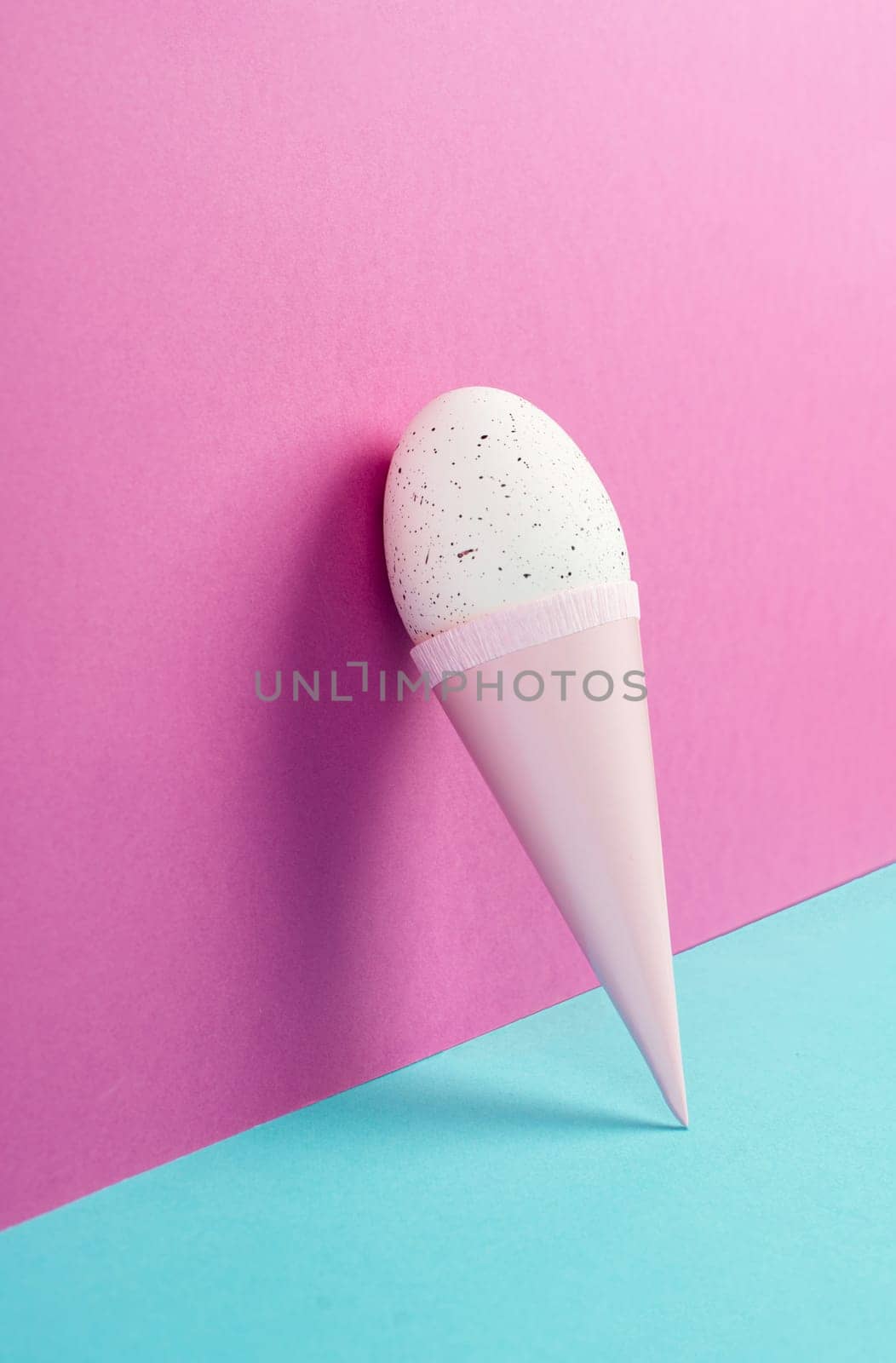 Ice cream cone with an egg, pink and blue background, copy space, easter holiday, summer season, minimalism and creative concept, greeting card