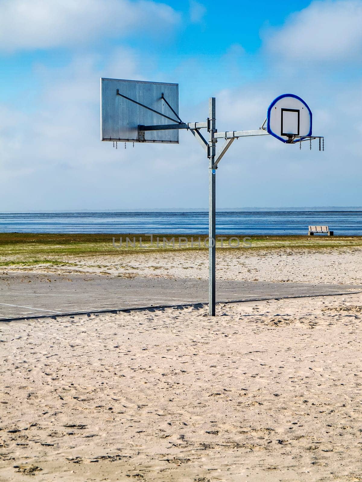 Half side view of a two-sided street basketball hoop mast on the North Sea beach in Harlesiel Ostfriesland in front of a blue sky in vertical orientation.