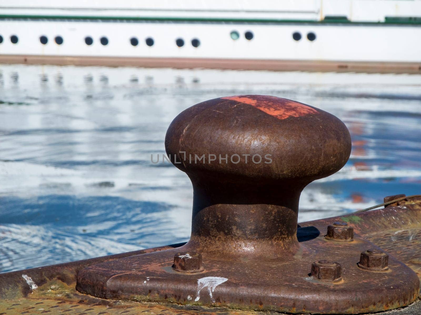 Low angle closeup of a steel bollard in Carolinensiel harbor with island ferry in blurred background in daylight and sunshine.