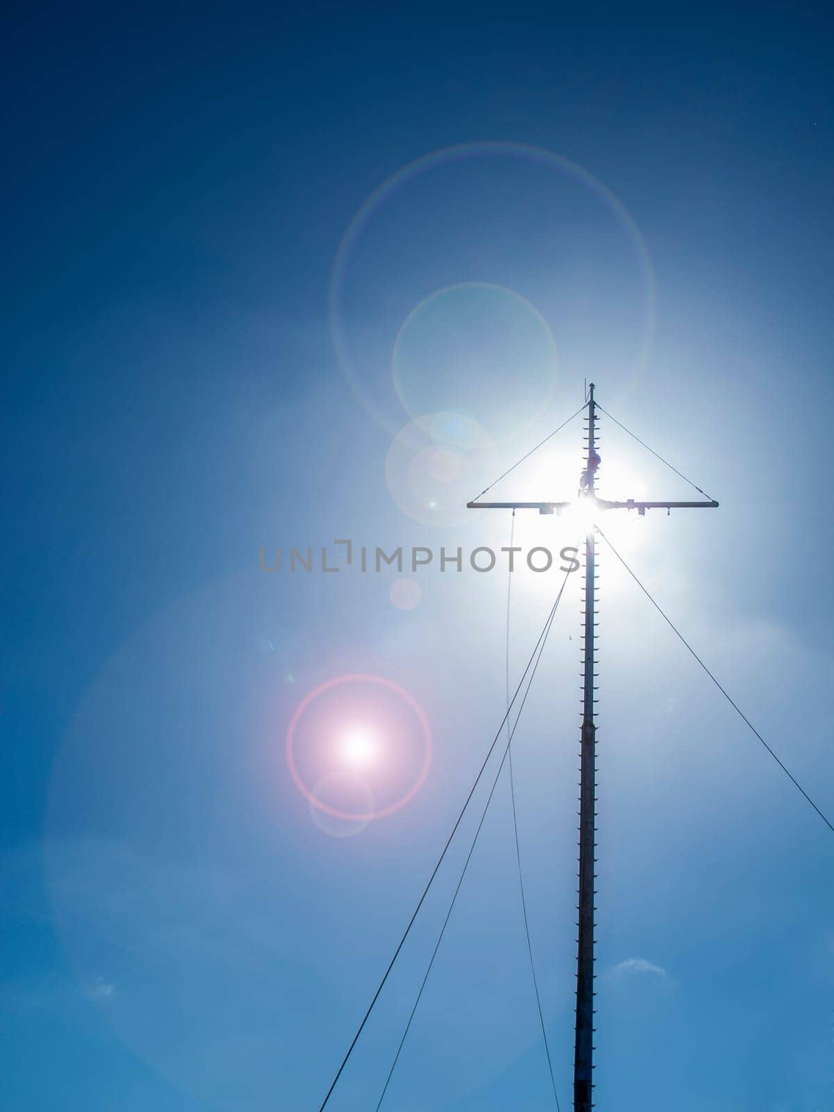 The radio mast obscuring the sun in the outshined backlight and lens flares in a blue sky in Carolinensiel Ostfriesland.