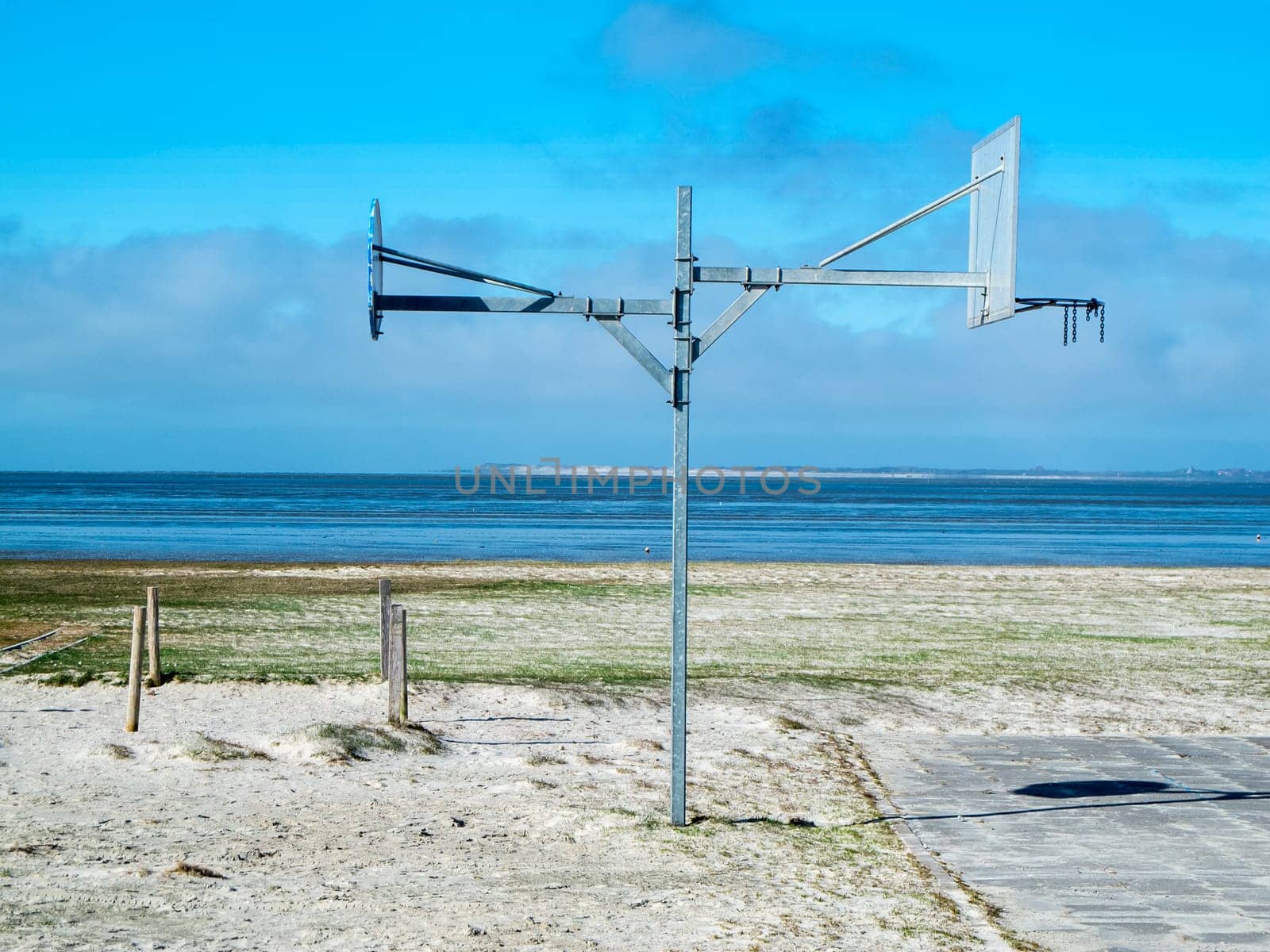 Side view of a double-sided street basketball hoop mast on the North Sea beach in Harlesiel Ostfriesland in front of a blue sky.