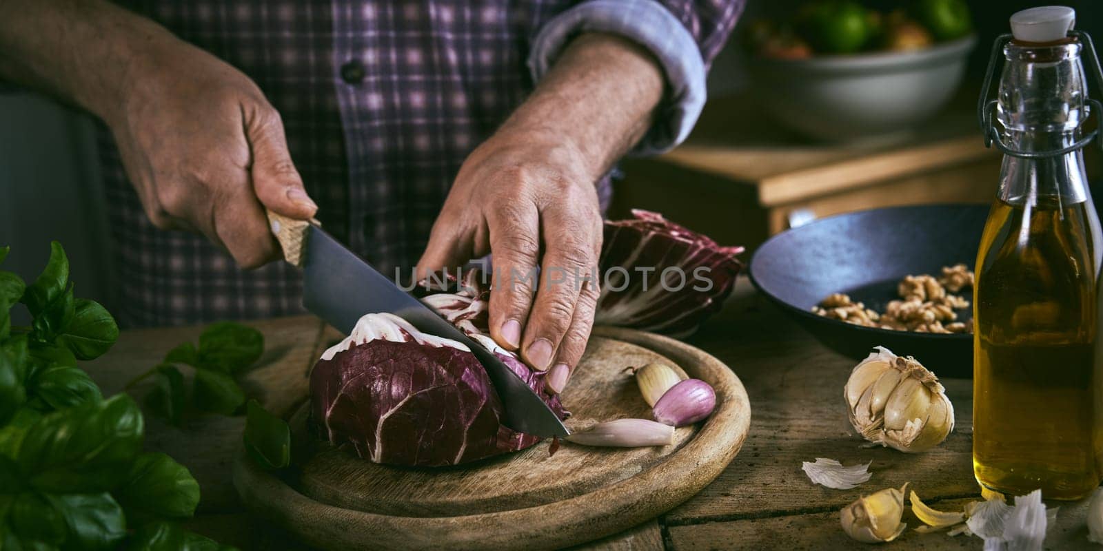 High angle of anonymous male in checkered shirt chopping ripe red cabbage with sharp knife near fresh cooking ingredient during lunch preparation at home