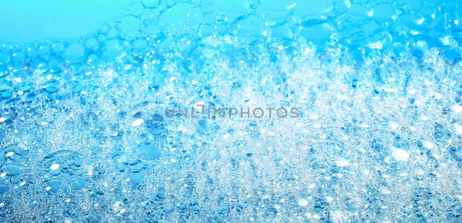 Background with fragile bubbles of white soap foam covering surface of bright blue water
