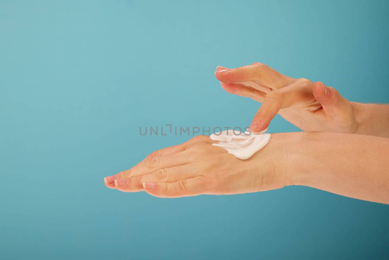 Unrecognizable female applying soft cream on hand with index finger during beauty routine against turquoise background