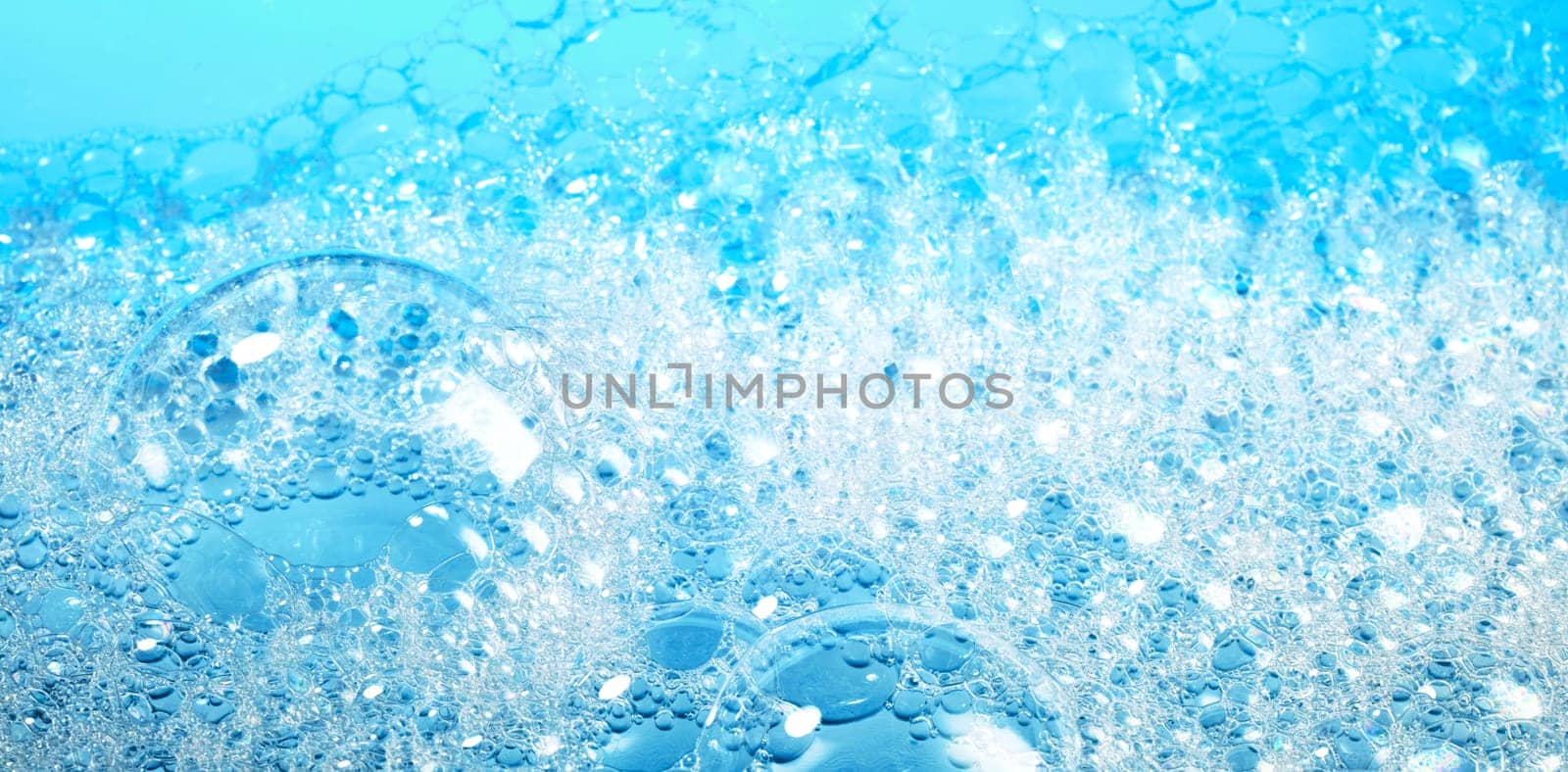 Wide angle of closeup transparent bubbles of soap foam covering surface of bright blue water