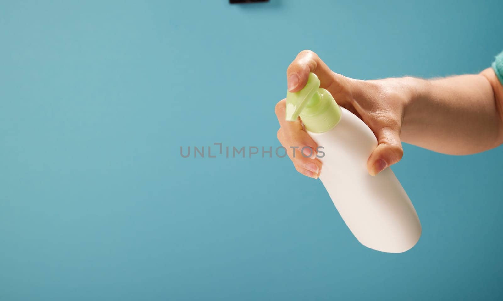 Unrecognizable woman pushing dispenser to apply soap from bottle during hygienic routine against turquoise background.
