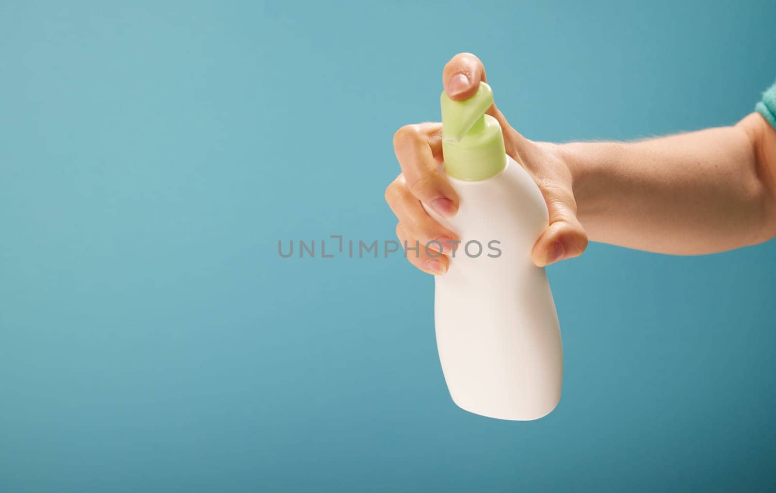 Unrecognizable female pressing dispenser on bottle of soap during hygienic routine against turquoise background