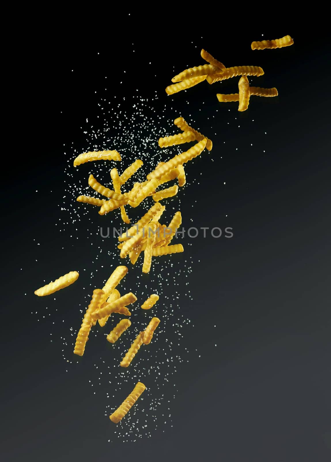 Flying pommes or french fries with salt on a dark background for takeaway advertising and burger shops