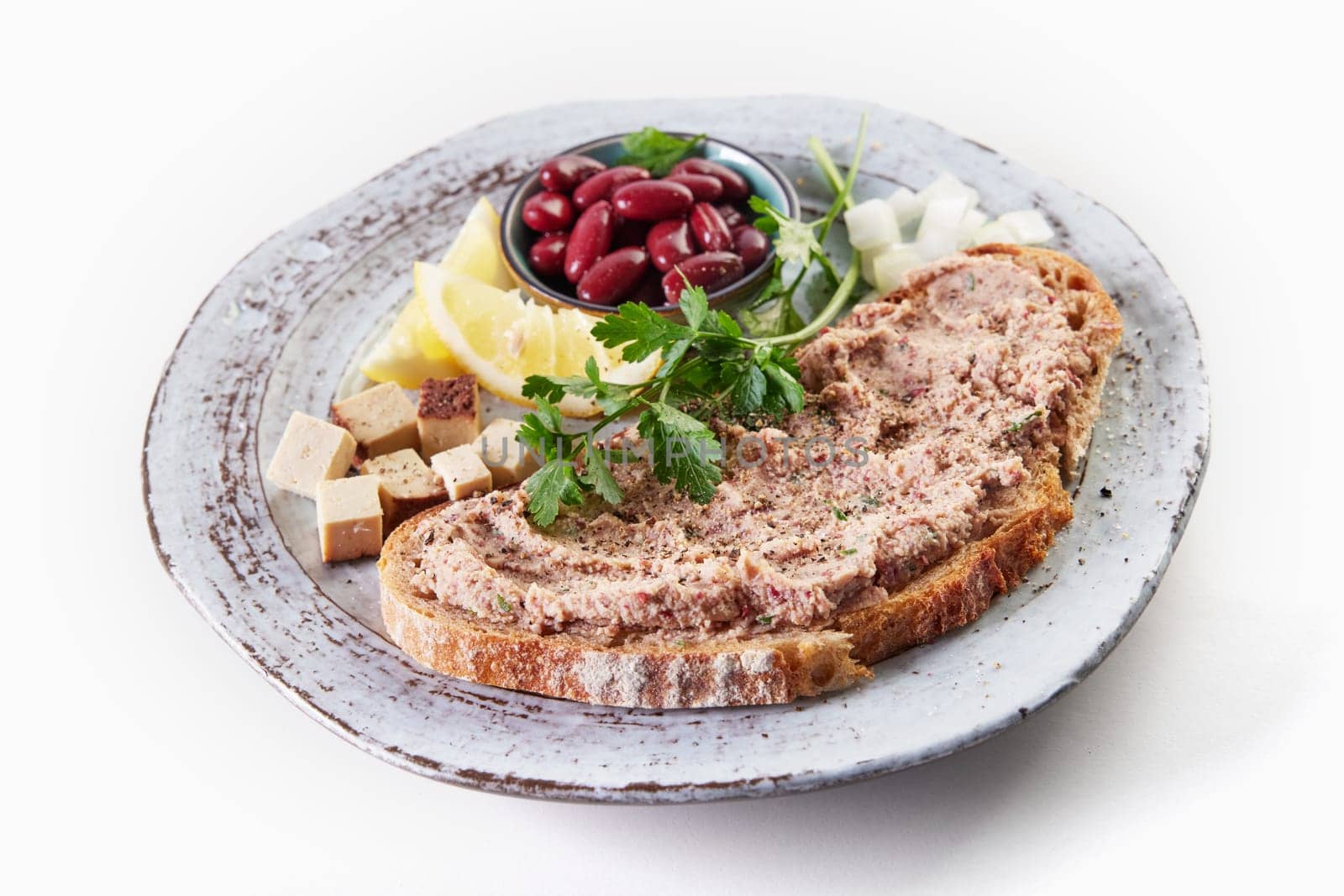From above of appetizing toast with homemade vegetarian liverwurst pate served on plate with bowl of red beans cubed cheese and lemon on white background