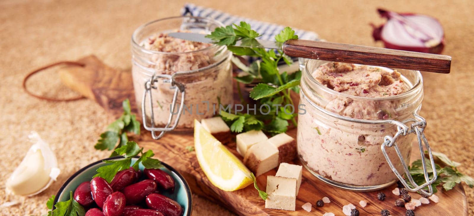 From above of delicious vegetarian liverwurst in pint jars with lemon slices and fresh parsley served on wooden board near bowl of marinated red beans in kitchen
