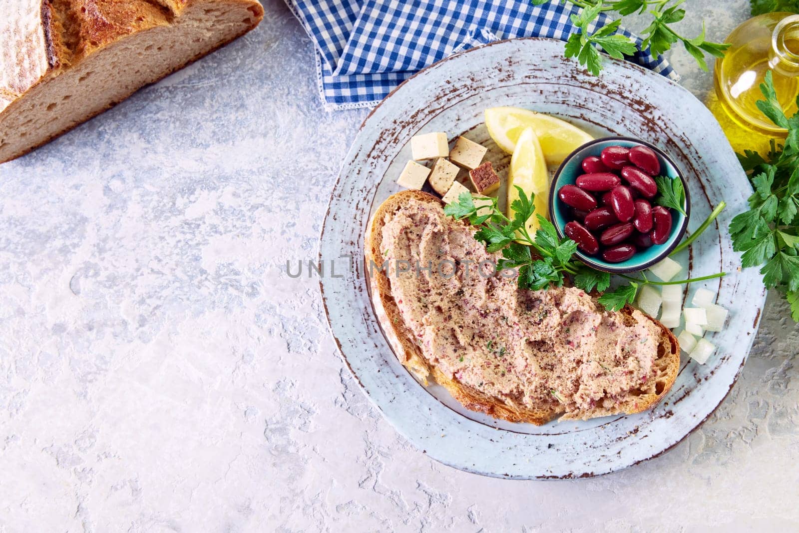 Top view of yummy bruschetta with vegetarian liverwurst pate served on plate with red beans cubed cheese and sliced lemons on table near carafe of olive oil and bread