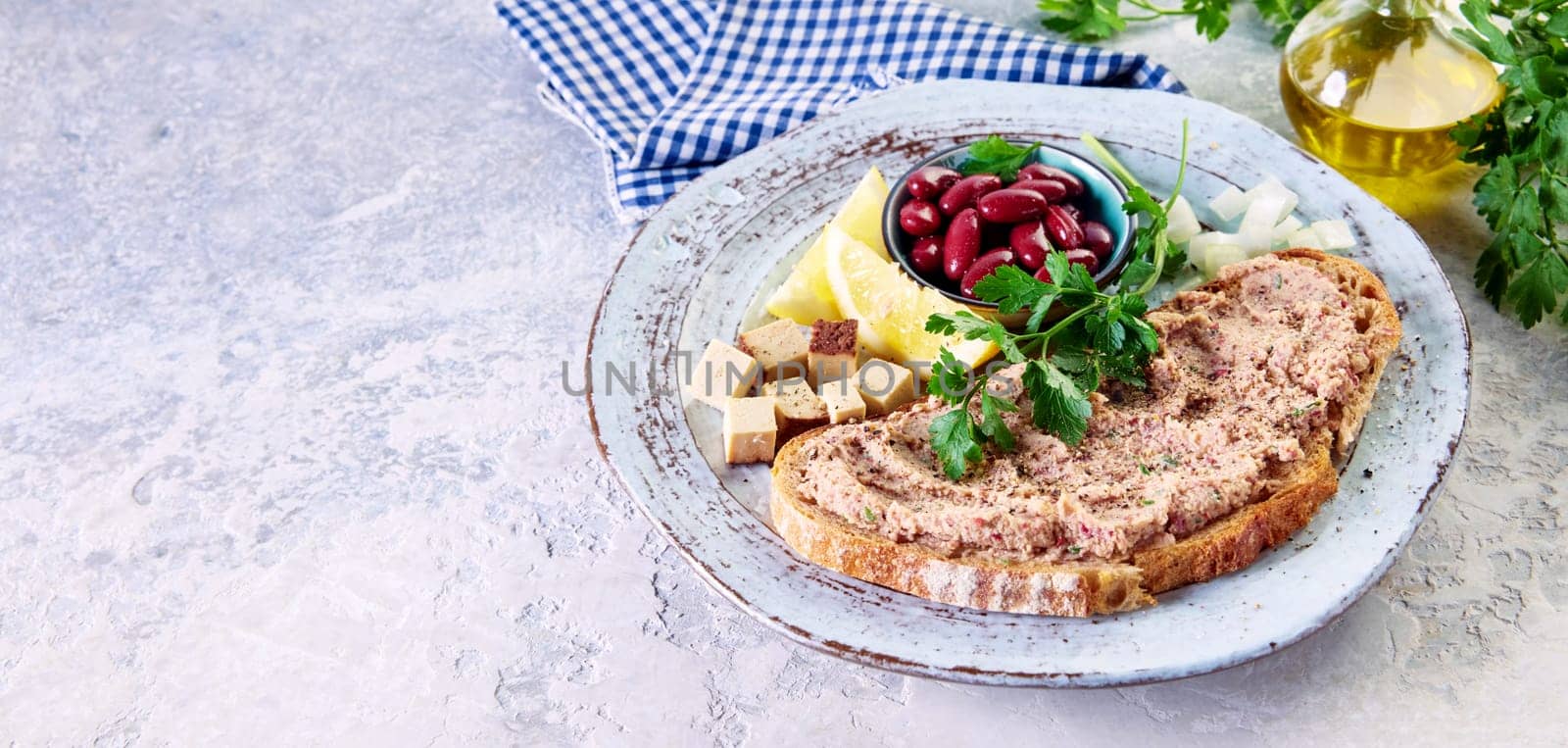 From above of yummy crunchy bread with homemade vegetarian liverwurst pate served on plate with bowl of kidney beans sliced lemons and cheese on table in kitchen