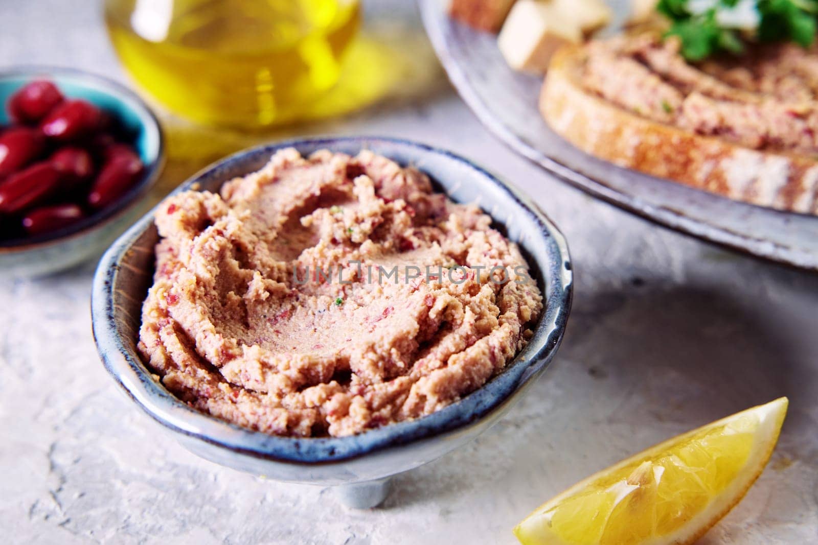 From above of delicious homemade kidney bean liverwurst pate in small ceramic bowl placed on table near plate of toast carafe of olive oil and sliced lemon in kitchen