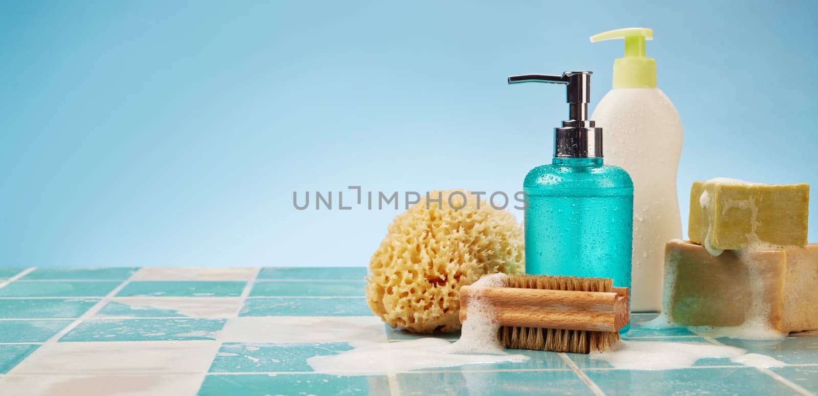 Wide angle of bottles and pieces of soap placed on wet tiled surface near zero waste sponge and brush against blue background