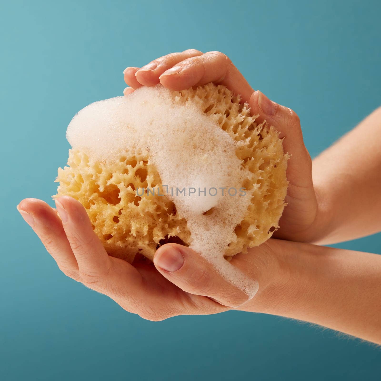 Hand of anonymous person holding foamy sponge on blue background