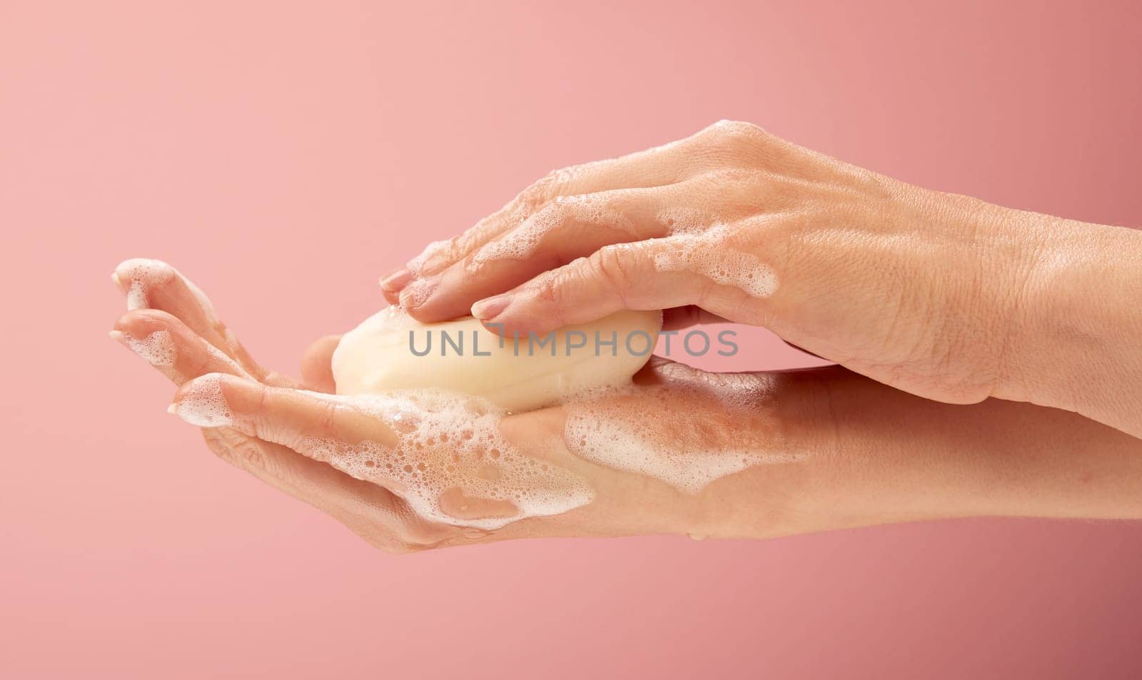 Young female hands cleaning hands with a natural soap with foam on feminine background.