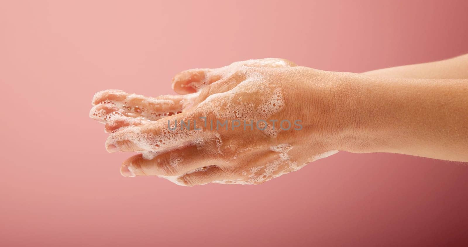 Woman s hands washing with soap, foam and water on bright pink background for healthcare and bath concepts.