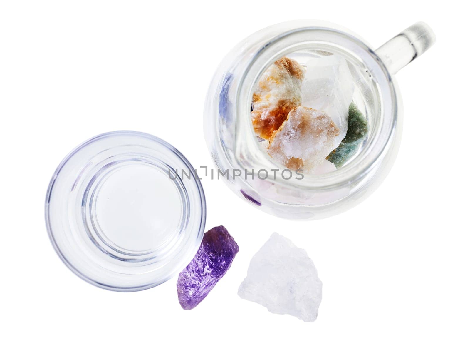 Top view set of various esoteric mineral water stones fro fresh water placed in glass jug near cup isolated on white background