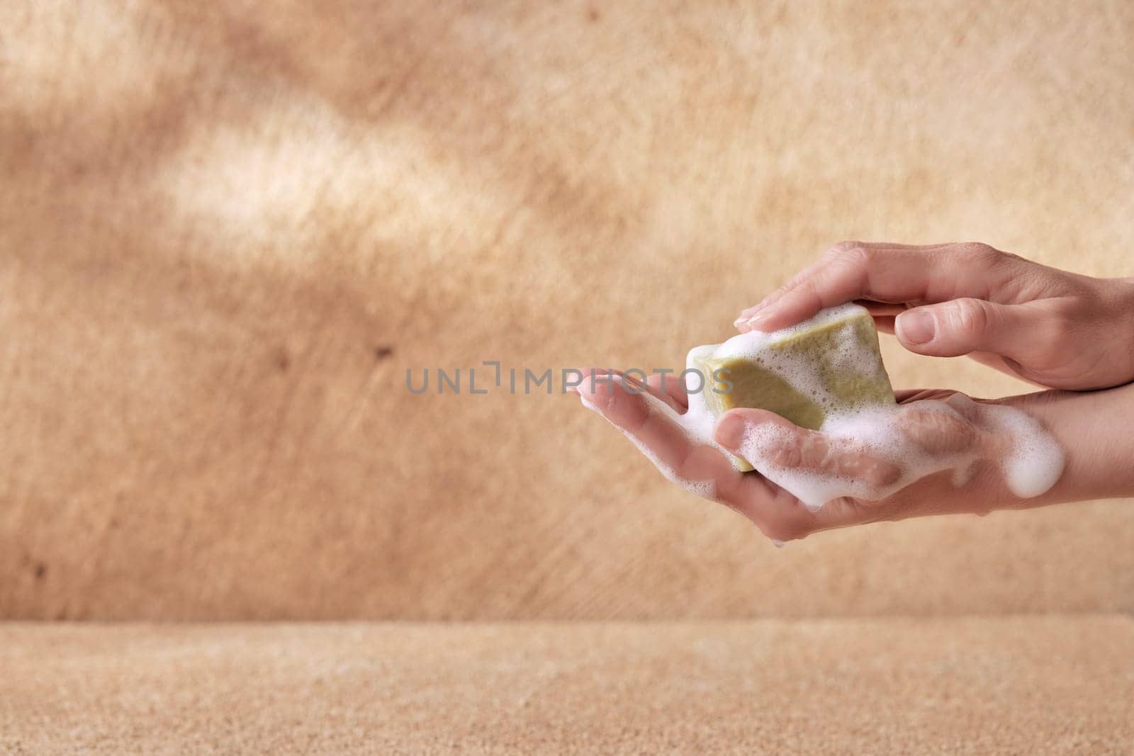 Sensitive hands of female holding soap with foam on brown background for skin and health care conceptual designs with copyspace.