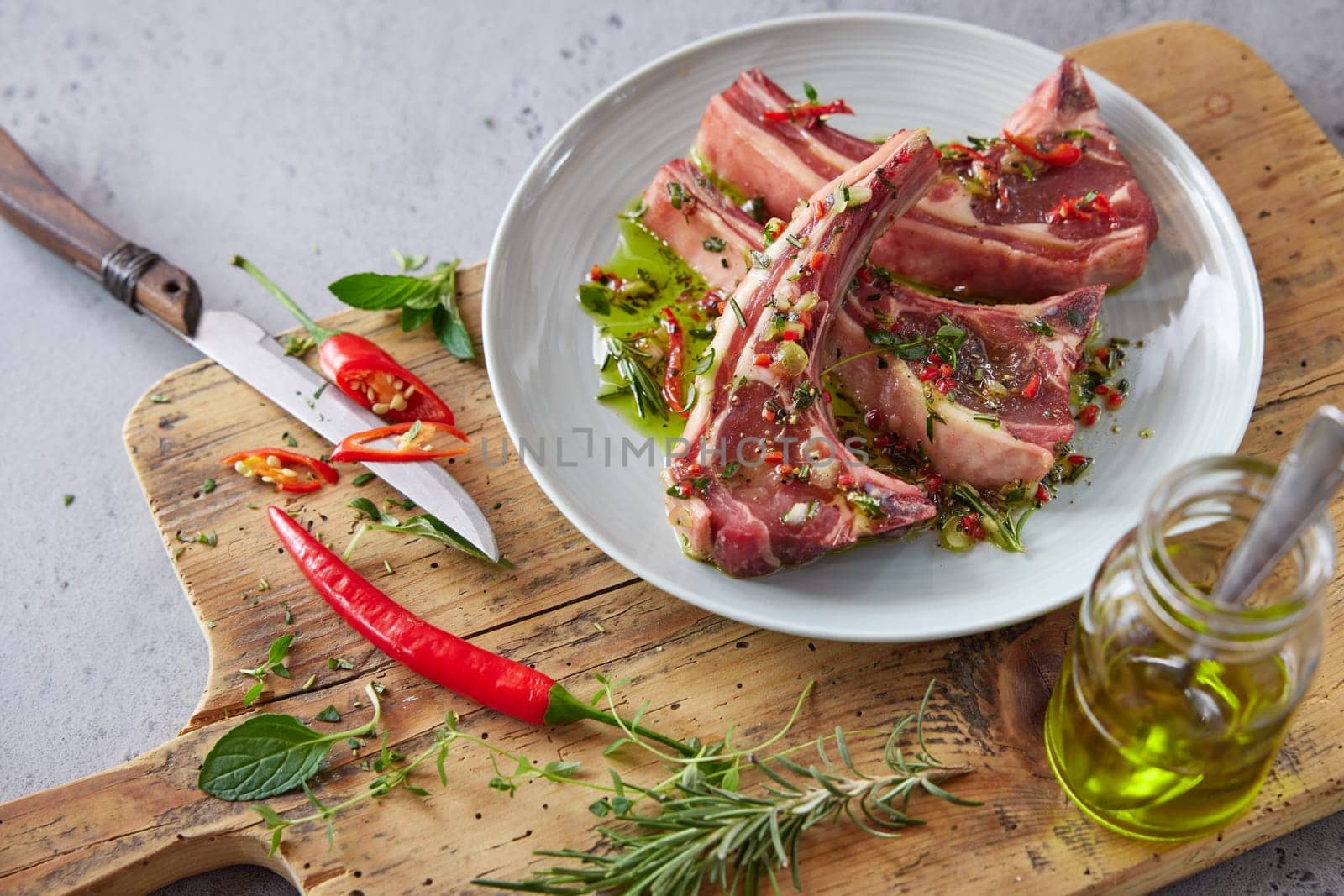 From above of plate with raw lamb chops placed on wooden chopping board with greens and hot pepper in kitchen