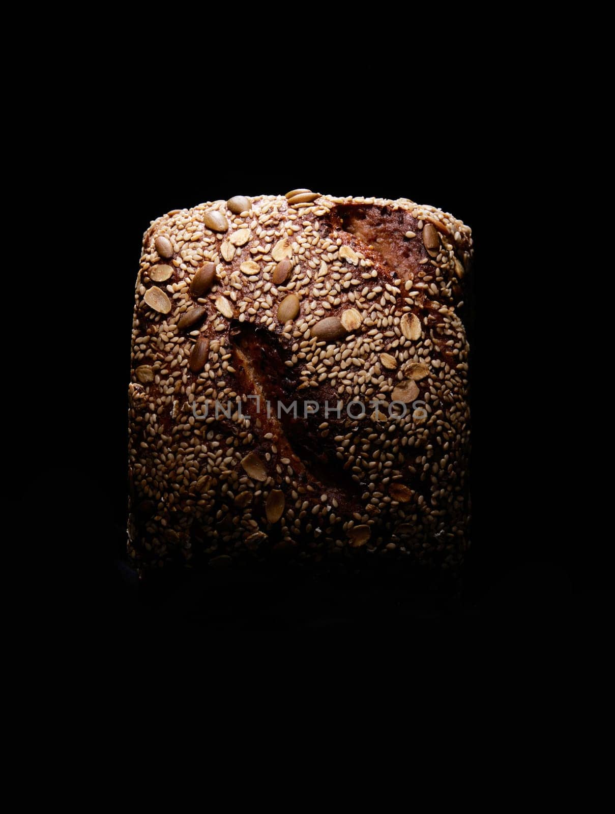 Top view of square shaped baked loaf of farmers bread with grains placed on black background in studio with dim light