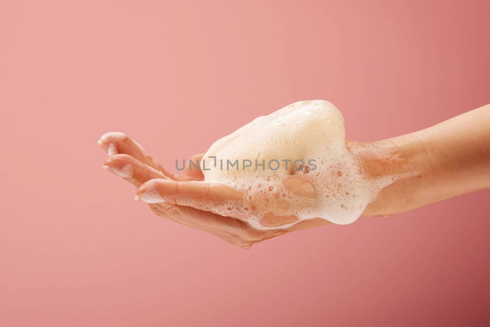 Hand with soap and foam on bright pink background for healthcare concepts.