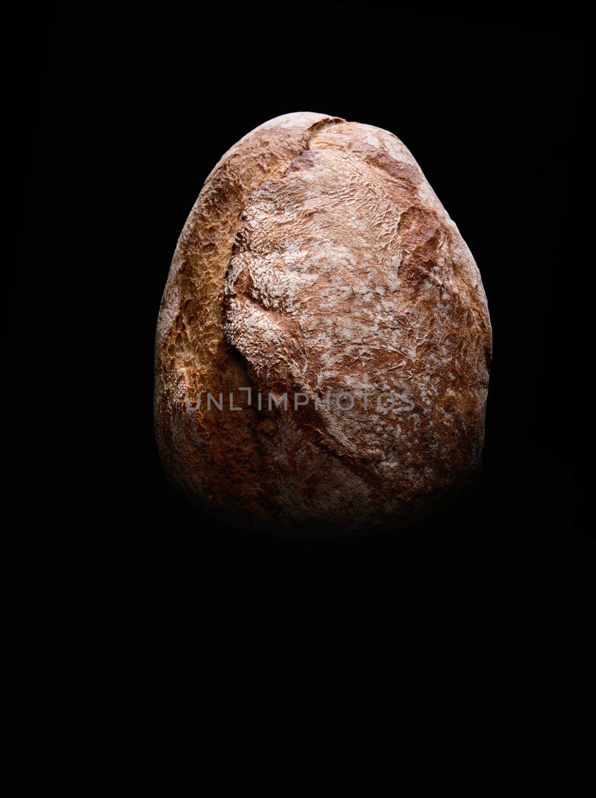 Top view of whole loaf of bread with crispy brown crust placed on black background in studio with dim illumination
