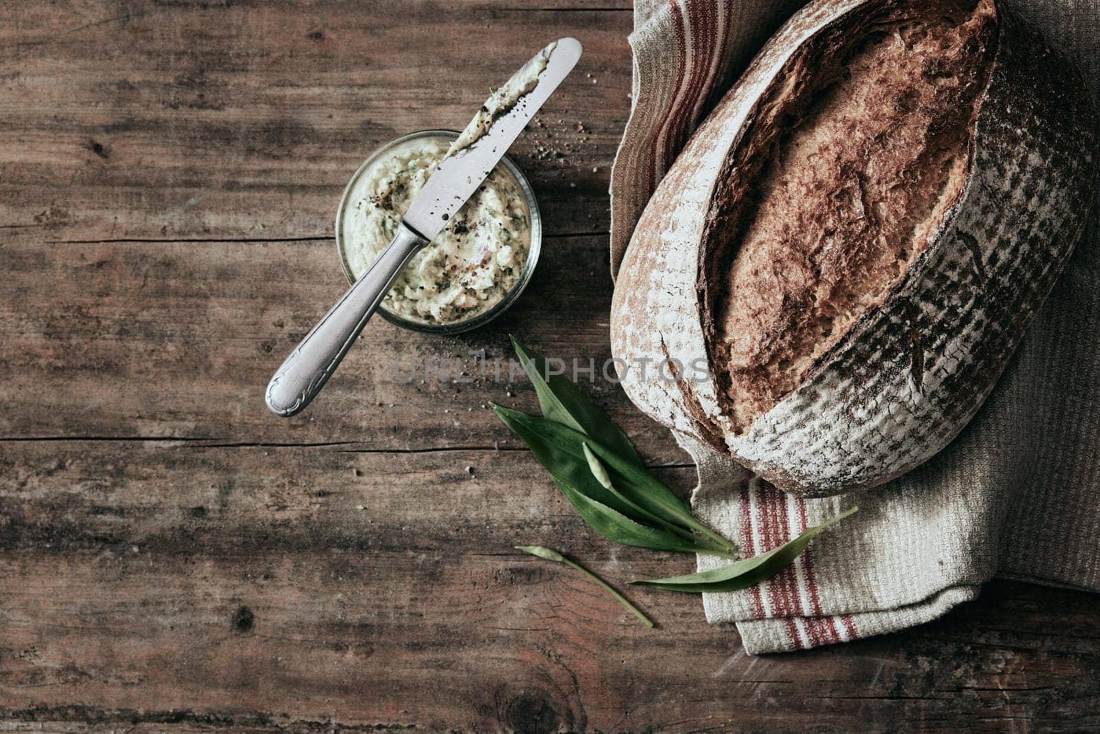 Top view of freshly baked loaf of bread placed on wooden table with jar of lard and towel in light kitchen