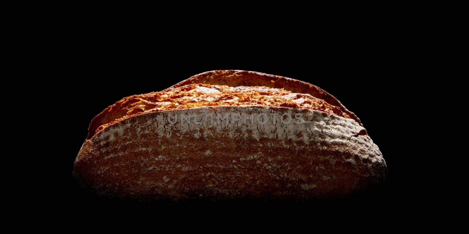 Whole loaf of tasty freshly baked farmers bread with crust covered with flour placed on black background in dark studio