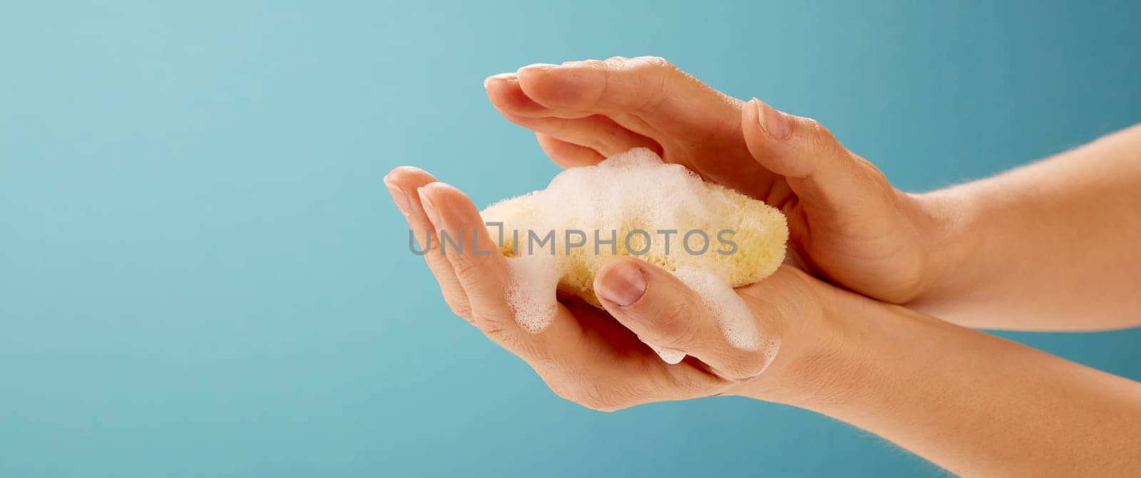 Crop hand of anonymous female applying moisturizing sponge on blue background in studio