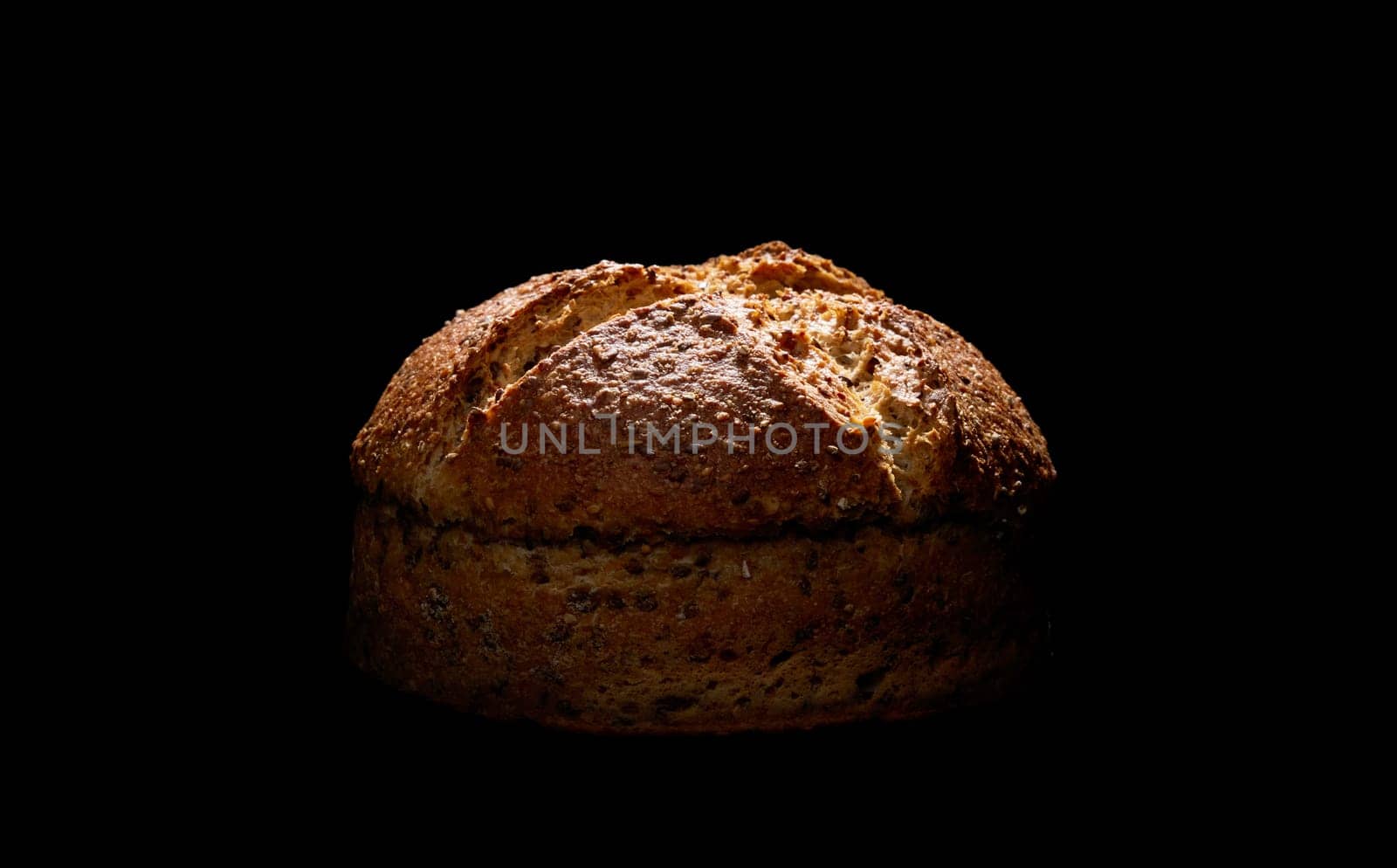Loaf of tasty freshly brown baked bread with seeds placed in darkness on black background in dark studio with dim light