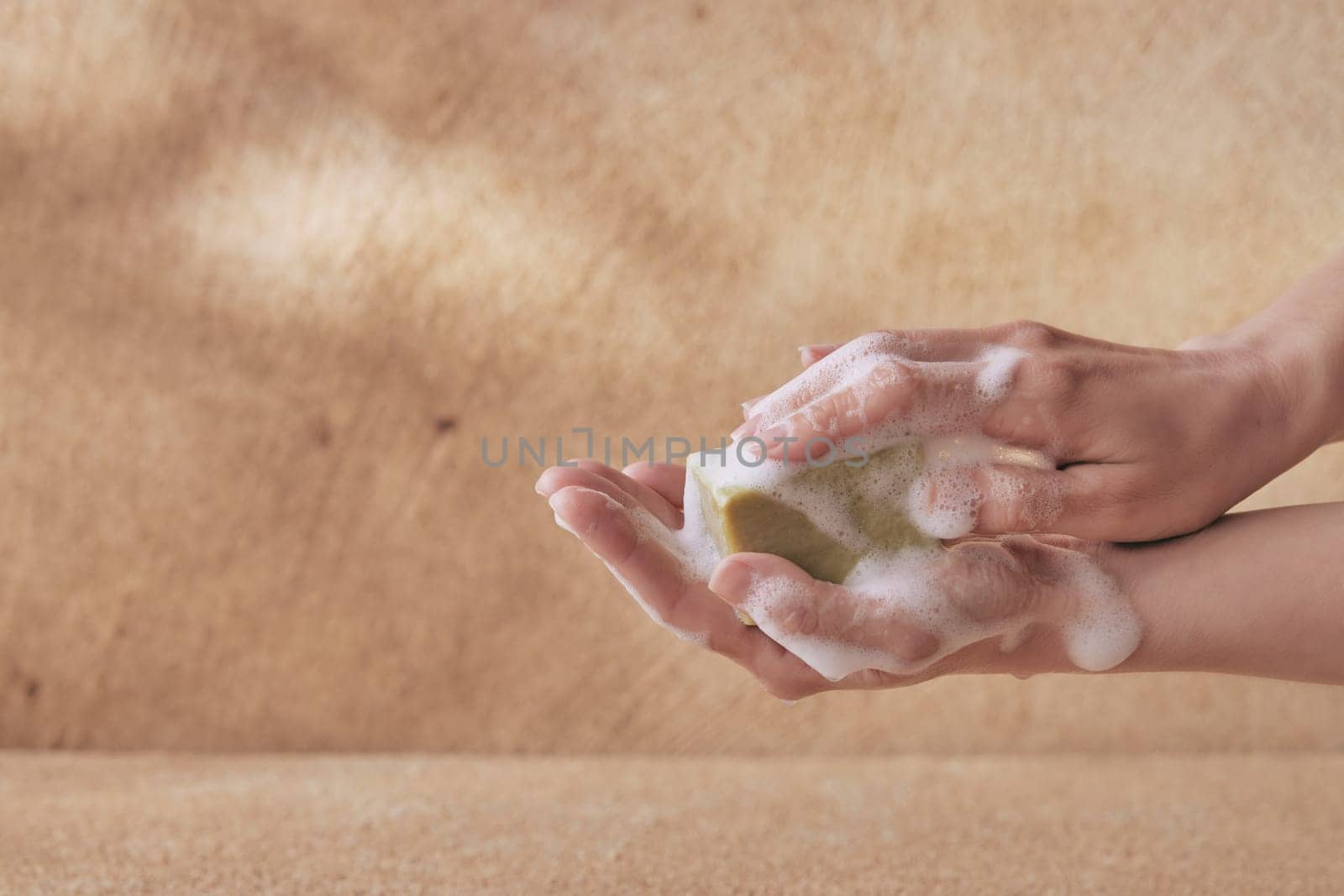 Crop female hand holding olive soap with foam with copyspace on brown background for healthcare and washing concepts