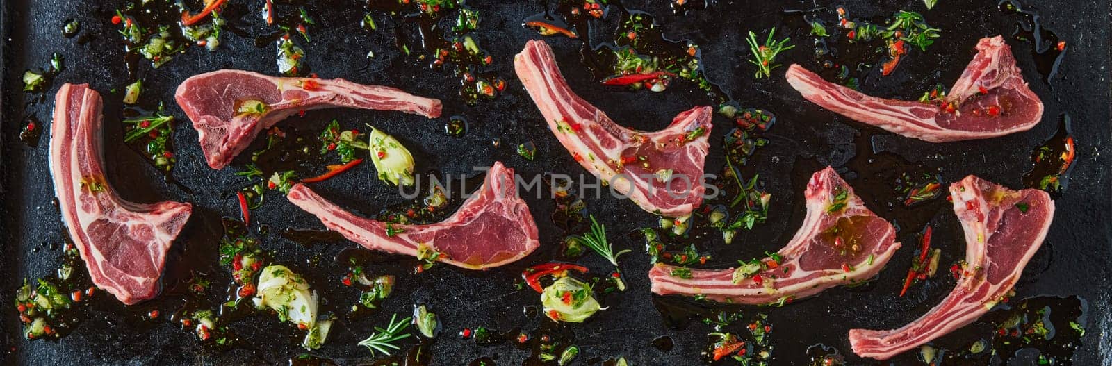 Top view panorama of fresh raw lamb chops and chopped green with chili pepper on black background in light kitchen