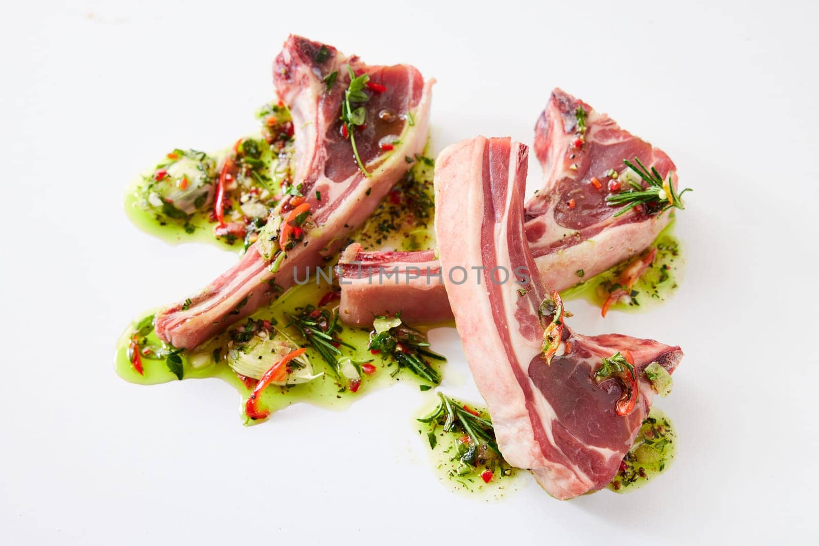 From above of uncooked lamb chops placed on white background with oil and chopped greens with garlic in light kitchen