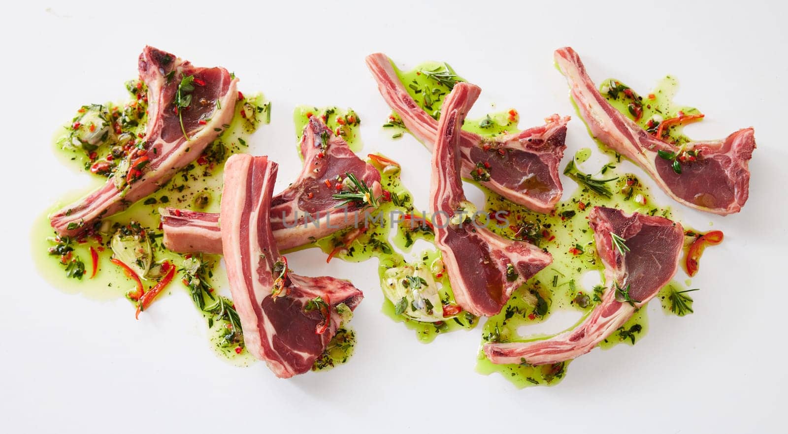 Top view of fresh raw lamb chops in marinate with oi and greens placed on white background in light kitchen