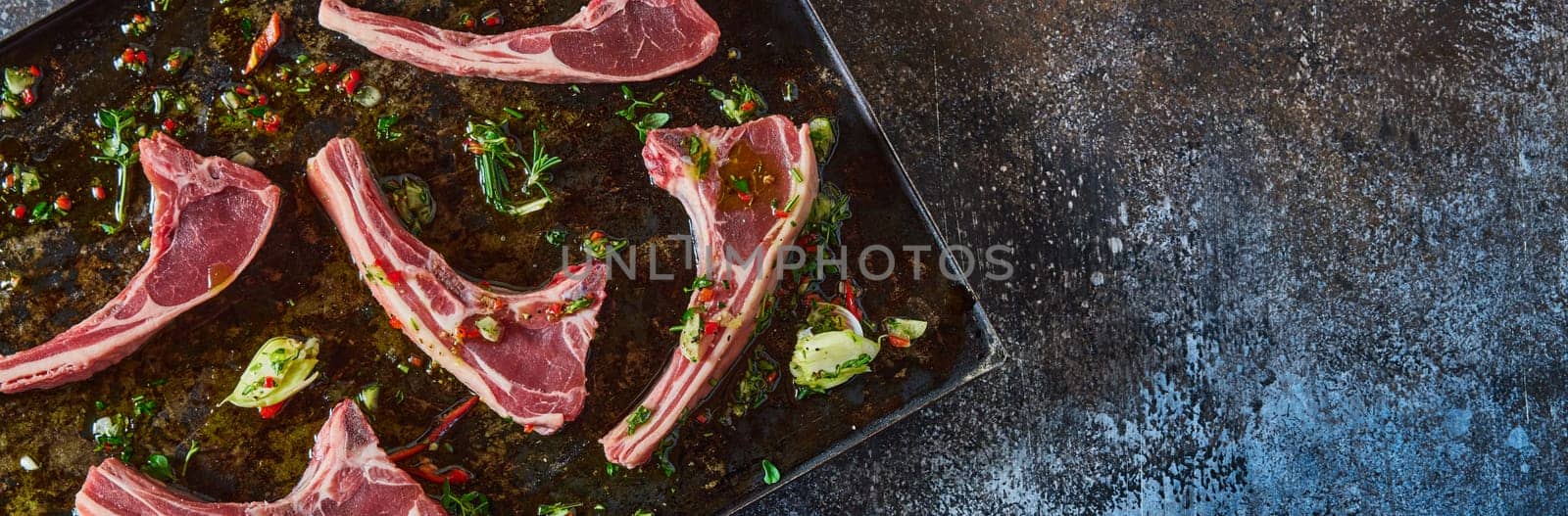 From above panorama of uncooked fresh lamb chops with chopped green placed on baking pan on table in light kitchen