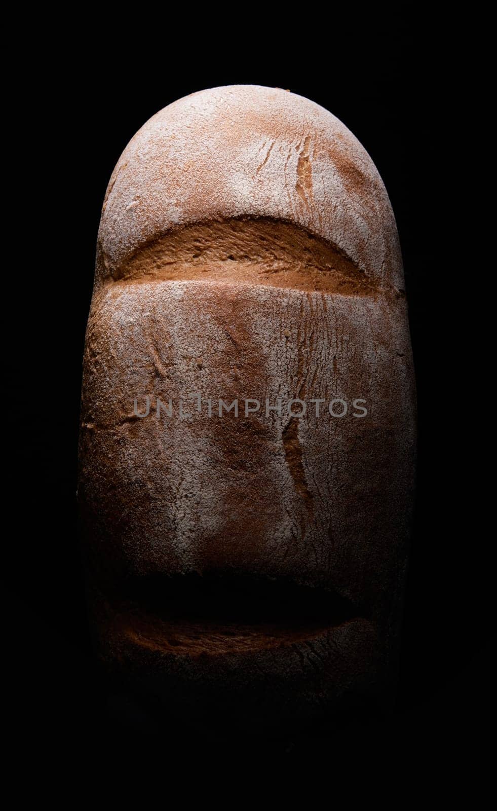 Top view of delicious freshly baked mixed wheat brown bread placed on black background in dark studio with dim illumination